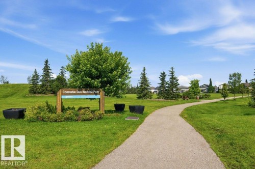 Expansive green space featuring a paved walking path, mature trees, and a wooden park sign - #17 7293 South Terwillegar Dr Nw, Edmonton, AB - Outdoor With View