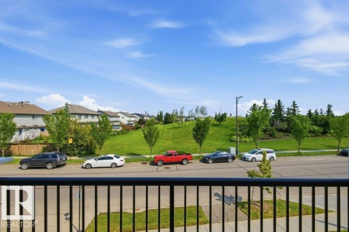 Balcony with black metal railing overlooking a residential street and a verdant hill with mature trees - #17 7293 South Terwillegar Dr Nw, Edmonton, AB - Outdoor With View