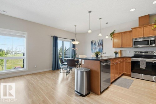 Kitchen featuring wood cabinetry, stainless steel appliances, dark countertops, and a subway tile backsplash - #17 7293 South Terwillegar Dr Nw, Edmonton, AB - Indoor Photo Showing Kitchen