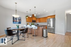 Open-concept kitchen and dining area featuring light wood-finish flooring, a kitchen island with pendant lighting, stainless steel appliances, and wood cabinetry - 