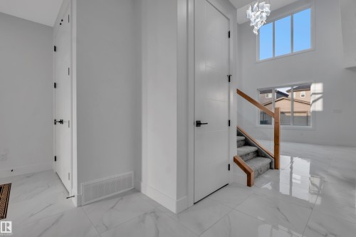 Entryway featuring polished tile flooring, a contemporary chandelier, two-story windows, and a staircase with wood banister and carpeted treads - 4005 39 Street, Beaumont, AB - Indoor Photo Showing Other Room