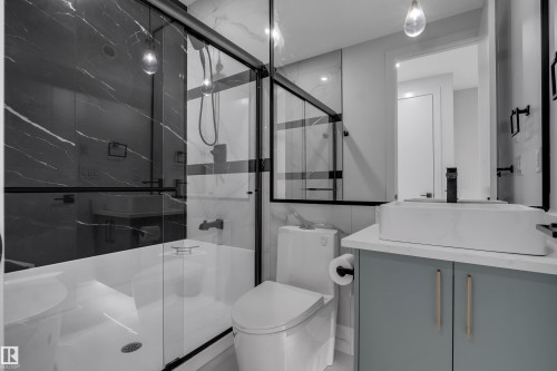Modern bathroom featuring a glass-enclosed shower-tub combination with black marble-finish wall tiling - 4005 39 Street, Beaumont, AB - Indoor
