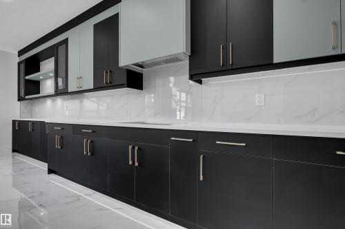 Modern kitchen featuring extensive dark cabinetry with gold-tone hardware, white countertops, and a white marble-look backsplash - 4005 39 Street, Beaumont, AB - Indoor Photo Showing Kitchen