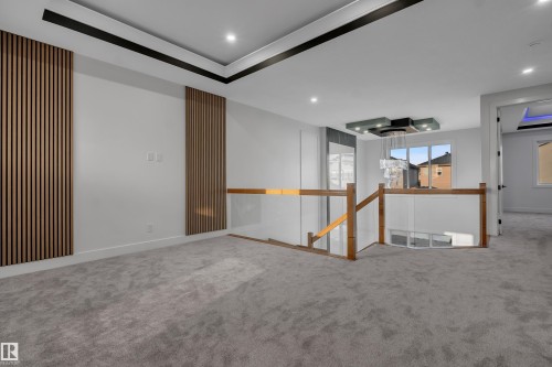 Upper-level landing featuring textured wood paneling, recessed lighting, a contemporary chandelier, a wood and glass railing system, and plush carpeting - 4005 39 Street, Beaumont, AB - Indoor Photo Showing Other Room