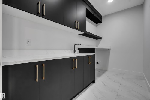 Laundry space featuring black cabinetry with gold-toned hardware, white countertops, and a black faucet - 4005 39 Street, Beaumont, AB - Indoor Photo Showing Other Room