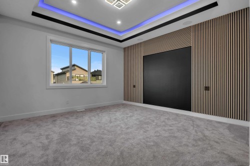 Contemporary room featuring a recessed tray ceiling with integrated lighting, a large window, light gray carpeting, and a wood-slat accent wall with a dark central panel - 4005 39 Street, Beaumont, AB - Indoor Photo Showing Other Room