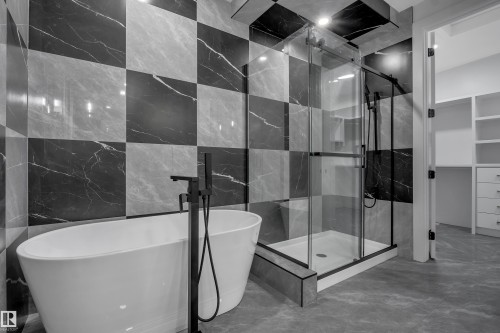 Bathroom featuring checkerboard-patterned wall tiles in black and gray, a freestanding white soaking tub with a matte black floor-mounted faucet, and a glass-enclosed shower with matte black hardware - 4005 39 Street, Beaumont, AB - Indoor Photo Showing Bathroom
