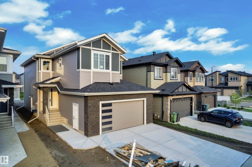 Modern two-story residence featuring a gray exterior with stone accents, a two-car garage with horizontal paneling, a concrete driveway, and a prominent front entry with white steps - 4005 39 Street, Beaumont, AB - Outdoor With Facade