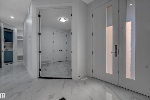 Entryway featuring large format white tile flooring with grey veining, a white door with frosted glass inserts, and a contemporary handle set - 4005 39 Street, Beaumont, AB - Indoor Photo Showing Other Room