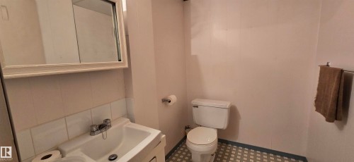Functional bathroom featuring a ceramic pedestal sink with chrome fixtures, white subway tile wainscoting, a ceramic toilet, and geometric patterned tile flooring - 5706 52 Street, Vegreville, AB 
