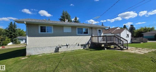 Split-level residence featuring a spacious rear lawn with mature landscaping, a composite deck with sturdy railings, and a two-tone exterior with stucco and vinyl siding - 5706 52 Street, Vegreville, AB 
