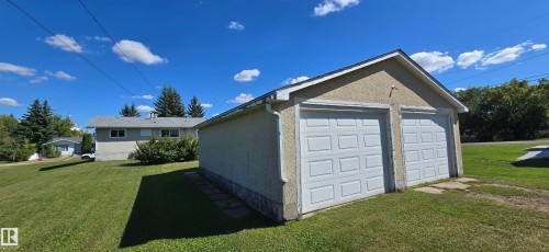 Spacious two-car garage with white panel doors, concrete foundation, and gable roof design - 5706 52 Street, Vegreville, AB 