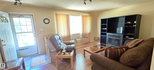 Bright, open living area featuring wood-finish flooring, large windows with natural light, built-in entertainment cabinetry with shelving, and a fireplace with surround - 5706 52 Street, Vegreville, AB 