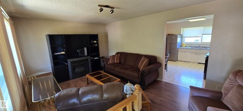 Spacious living area featuring wood-finish flooring, built-in entertainment cabinetry with shelving, and large windows providing natural light - 5706 52 Street, Vegreville, AB 