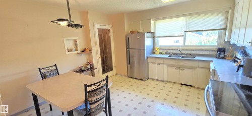 Bright, open kitchen featuring stainless steel appliances, ample cabinetry with light finishes, ceramic tile flooring, and abundant natural light from multiple windows - 5706 52 Street, Vegreville, AB 