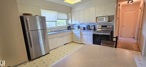 Bright, open kitchen featuring stainless steel appliances, white cabinetry with ample storage, tile flooring, and a spacious countertop work surface with large windows allowing natural light throughout the room - 5706 52 Street, Vegreville, AB 