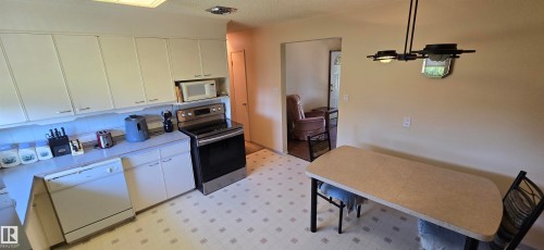 Spacious open-concept kitchen and dining area featuring white cabinetry, stainless steel appliances, tile flooring, and pendant lighting - 5706 52 Street, Vegreville, AB 