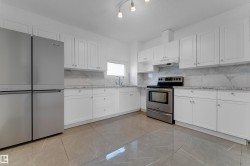 Kitchen featuring white shaker-style cabinetry, stainless steel appliances, stone countertops, a tile backsplash, and large format tile flooring - 