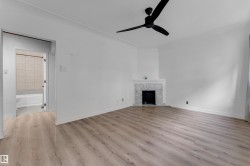 Wood-finish flooring, white walls, black ceiling fan, white fireplace with marble surround, and an adjacent bathroom with a white tub and tiled walls - 