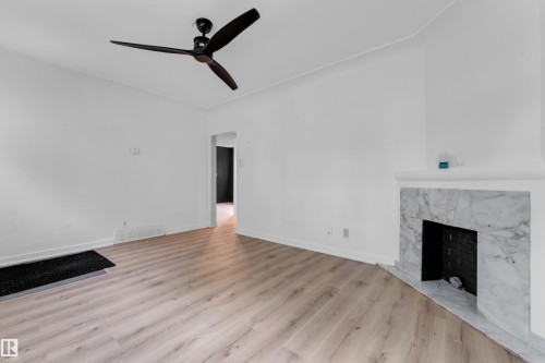 Wood-finish flooring throughout, white walls, ceiling fan, fireplace with white marble surround, and an open doorway - 12116 81 Street Nw, Edmonton, AB 