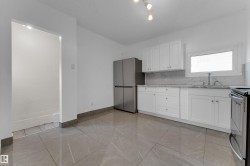 Grey-toned tile flooring, white shaker cabinetry, stainless steel appliances, white countertop, and a white tile backsplash - 