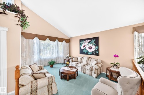 Bright, sun-filled living room featuring vaulted ceilings, large bay window with custom valance, wood-finish flooring, and mint-green carpet throughout - 4327 49 Street Nw, Edmonton, AB 