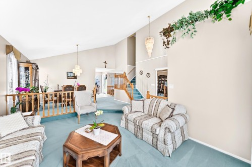 Vaulted ceilings with decorative light fixtures, a carpeted living area, a dining area with a wood railing, and a staircase with wood newels - 4327 49 Street Nw, Edmonton, AB 