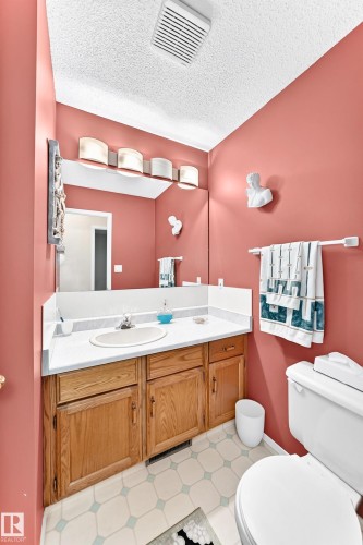 Spa-inspired bathroom showcasing warm coral walls, a wood-finish vanity with dual sinks and ample storage, white subway tile flooring, and polished chrome fixtures - 4327 49 Street Nw, Edmonton, AB 