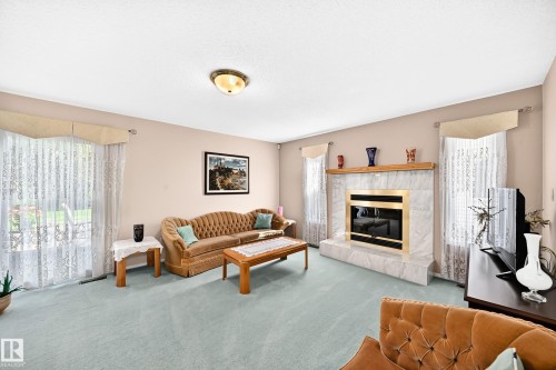 Spacious living room featuring a fireplace with built-in cabinetry, wood-finish flooring, recessed ceiling lighting, and glass sliding doors with sheer drapery treatments providing natural light throughout the space - 4327 49 Street Nw, Edmonton, AB 