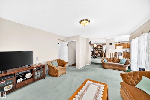 Spacious open-concept living area with plush seating arrangements, wood-finish media console with integrated storage, soft ambient ceiling lighting, and expansive light-filled layout enhanced by natural daylight from multiple windows - 4327 49 Street Nw, Edmonton, AB 
