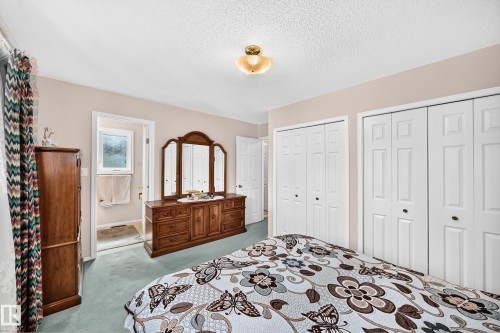 Spacious primary bedroom featuring dual walk-in closets with six-panel doors, wood-finish dresser with attached mirror, carpet flooring, and recessed ceiling lighting - 4327 49 Street Nw, Edmonton, AB 