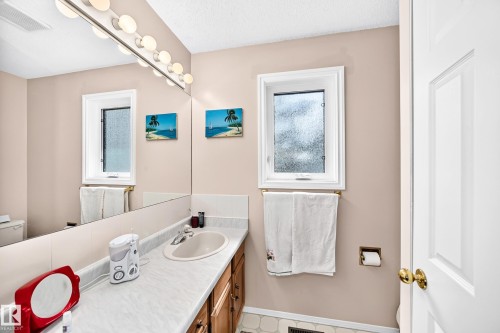Bright bathroom featuring dual windows with natural light, wood-finish vanity with white countertop, white subway tile wainscoting, polished brass hardware, and recessed lighting above the mirror - 4327 49 Street Nw, Edmonton, AB 