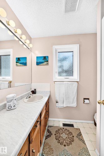 Bathroom featuring a vanity with an integrated sink, wood-finish cabinetry, and a large mirror with integrated lighting - 4327 49 Street Nw, Edmonton, AB 