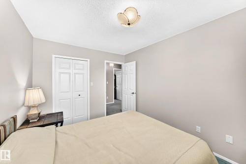 Serene primary bedroom showcasing neutral wall finishes, recessed ceiling lighting, dual closet doors with white six-panel styling, and a table lamp with pleated shade - 4327 49 Street Nw, Edmonton, AB 