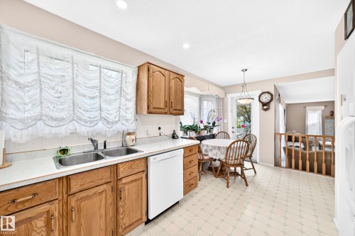 Bright kitchen featuring wood-finish cabinetry, white subway tile backsplash, and stainless steel sink with white dishwasher - 4327 49 Street Nw, Edmonton, AB 
