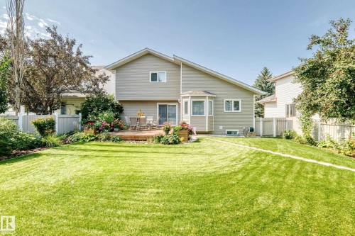 Expansive manicured lawn with mature landscaping, flowering garden beds, and wooden deck with seating area - 4327 49 Street Nw, Edmonton, AB 