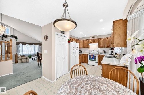 Open kitchen and dining area featuring wood-finish cabinetry, white appliances, tile flooring, and a pendant light fixture overhead - 4327 49 Street Nw, Edmonton, AB 