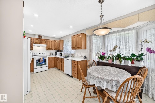 Kitchen with wood cabinetry, white appliances, recessed lighting, and a dining area with a bay window - 4327 49 Street Nw, Edmonton, AB 