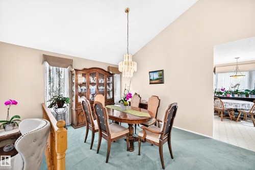 Elegant formal dining room featuring a round wood pedestal table, upholstered dining chairs, and a crystal chandelier pendant - 4327 49 Street Nw, Edmonton, AB 