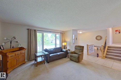 Spacious living room featuring a tile floor, large glass sliding doors with natural light, neutral wall finishes, and a wood-finish dresser - 14 Brunswick Crescent, St. Albert, AB 
