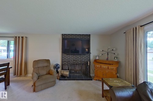 Spacious living room featuring a brick fireplace with dark tile surround, wood-finish flooring, large windows with natural light, and elegant drapery - 14 Brunswick Crescent, St. Albert, AB 