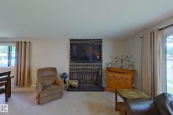 Spacious living room featuring a brick fireplace with dark tile surround, wood-finish flooring, large windows with natural light, and elegant drapery - 