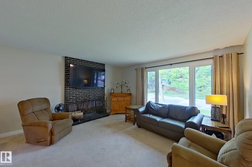 Spacious living room featuring neutral carpeting, a wood-burning fireplace with black surround, built-in cabinetry, and large sliding glass doors with dual-pane windows opening to outdoor space - 14 Brunswick Crescent, St. Albert, AB 