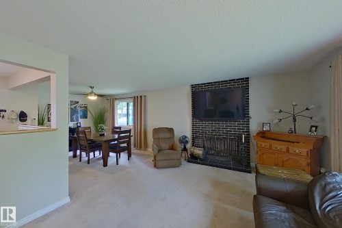 Spacious living area featuring neutral carpet flooring, a wall-mounted flat-screen television with black tile surround, a gas fireplace with decorative black tile facade, and abundant natural light from multiple windows - 14 Brunswick Crescent, St. Albert, AB 