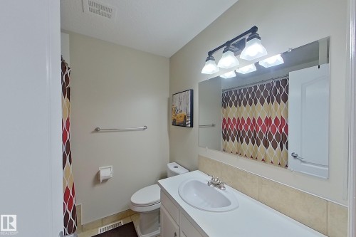 Bright bathroom featuring a white vanity with dual sink basins, ceramic tile backsplash in neutral tones, illuminated mirror with integrated lighting, and white cabinetry storage below the countertop - 14 Brunswick Crescent, St. Albert, AB 