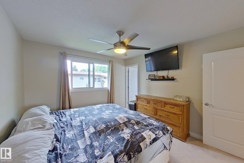 Bright secondary bedroom featuring a ceiling fan with integrated lighting, wood-finish dresser, large window with natural light, and neutral carpeting throughout - 14 Brunswick Crescent, St. Albert, AB 