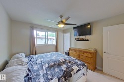 Bright secondary bedroom featuring a ceiling fan with integrated lighting, wood-finish dresser, large window with natural light, and neutral carpeting throughout - 