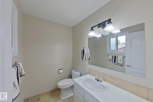 Bright bathroom featuring dual vanity with white cabinetry and wood-finish countertop, large framed mirror with integrated lighting, ceramic tile flooring, and updated fixtures throughout - 14 Brunswick Crescent, St. Albert, AB 