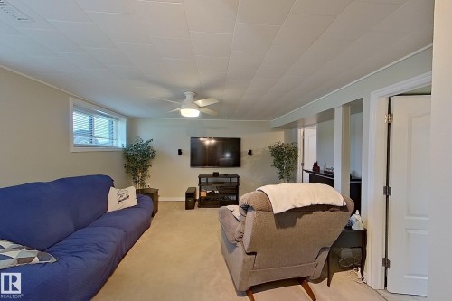 Finished basement recreation room featuring plush seating arrangements, wall-mounted entertainment system with surround sound speakers, neutral carpeting throughout, and multiple doorway access points - 14 Brunswick Crescent, St. Albert, AB 