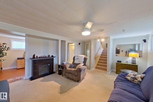 Spacious finished basement featuring carpeted flooring, a wood-burning fireplace with dark surround, recessed and ceiling-mounted lighting, built-in shelving, and direct access to wooden staircase - 14 Brunswick Crescent, St. Albert, AB 